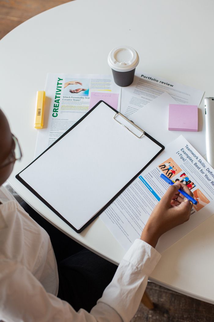 A person reviews documents at a desk with a blank clipboard and coffee cup.